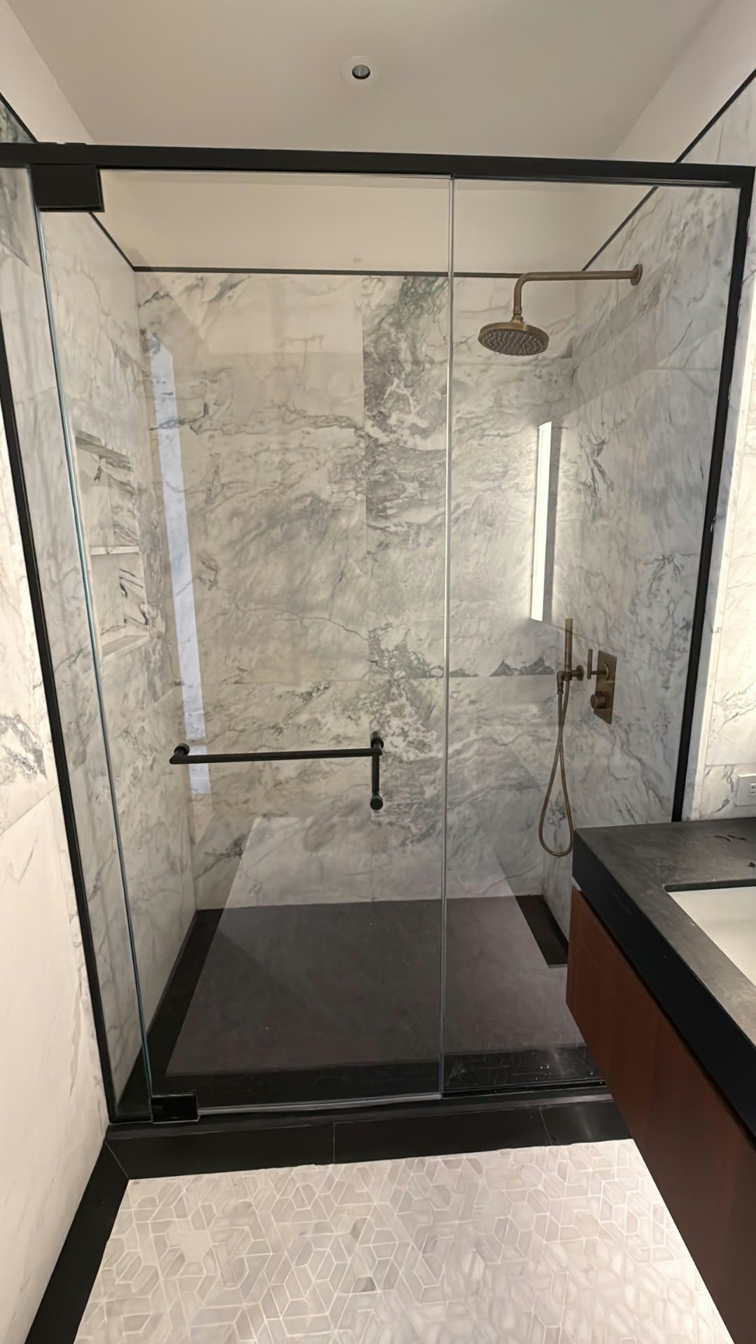Custom frameless glass shower enclosure with brass hardware and marble tile, New Jersey